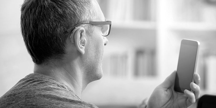 A man wearing glasses and a hearing aid looks at an iphone screen