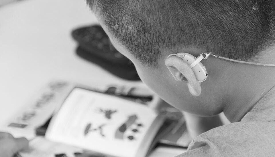 A boy reads a book wearing a hearing aid.
